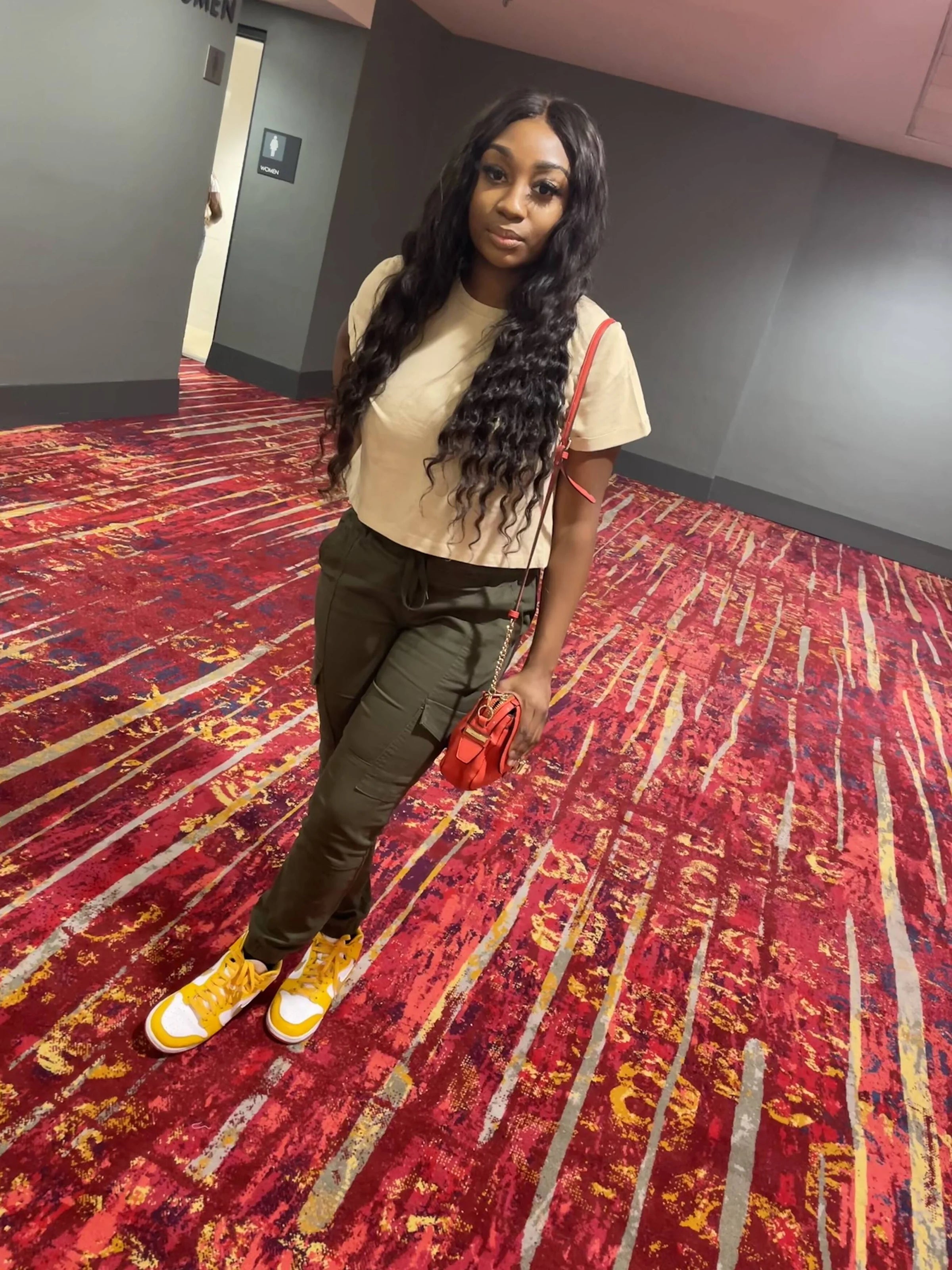 Woman standing on a red and gold patterned carpet in an indoor setting wearing a custom glue-less loose wave wig from WinkLilly beauty